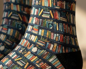 May include: A pair of crew socks featuring a dark blue background with a repeating pattern of horizontal bookshelves filled with colorful books, small potted plants, and decorative vases arranged in rows across the fabric.