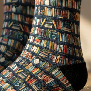 May include: A pair of crew socks featuring a dark blue background with a repeating pattern of horizontal bookshelves filled with colorful books and small potted plants. The design includes various book spine colors like red, yellow, green, and white.