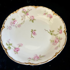 Könnte beinhalten: Kleine, weiße Porzellanschale mit gewelltem Rand und Goldrand. Zarte rosa Rosen und grüne Blätter sind um den Rand und die Mitte der Schale gemalt. Wahrscheinlich Vintage.