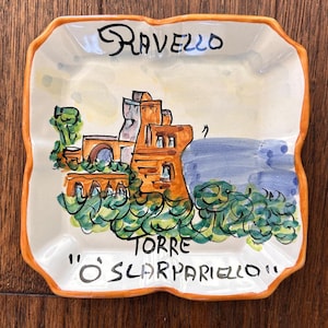 Może przedstawiać: Biały ceramiczny kubek z czarnym uchwytem i napisem "But First, Coffee" w stylu odręcznym. Kubek stoi na białej powierzchni. Kubek ma około 10 cm wysokości.