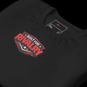 May include: Black t-shirt with a red and white graphic that reads "BUILT FOR RIVALRY" in a bold, stylized font. The design includes stars and a shield shape. The shirt has a crew neck and a tag.