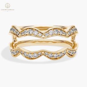 May include: Two gold-colored rings with a wavy design, each encrusted with small, clear gemstones. The rings are stacked, showcasing the intricate details of the jewelry. The brand name "CROWN JEWELZ" is visible in the upper left corner.