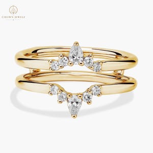 May include: Two gold rings with a diamond design. Each ring has a curved row of small diamonds and a larger pear-shaped diamond in the center. The rings are set against a white background. The brand name "CROWN JEWELZ" is in the upper left corner.
