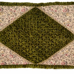 May include: A rectangular throw cushion featuring a central diamond-shaped panel of olive green velvet with a smocked, geometric pattern. The border is a cream-coloured fabric with a floral print, finished with a ruffled olive green velvet trim.