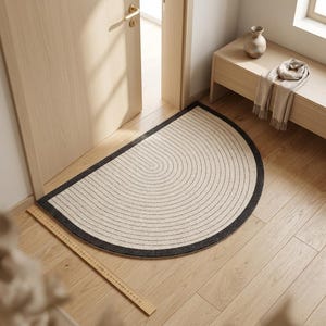 May include: A semi-circular floor mat featuring a cream-colored center with concentric black line patterns and a solid black border. A wooden ruler is placed along the edge, showing a measurement of approximately 30 inches in total length.