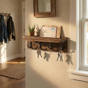 Könnte beinhalten: Ein an der Wand montierter Schlüsselhalter und Postorganizer aus dunklem Holz. Er verfügt über ein Regal mit einer kleinen Pflanze, einem Umschlag und einer Karte. Darunter befinden sich fünf Metallhaken mit Schlüsseln. Dunkelbraune Holzoberfläche.