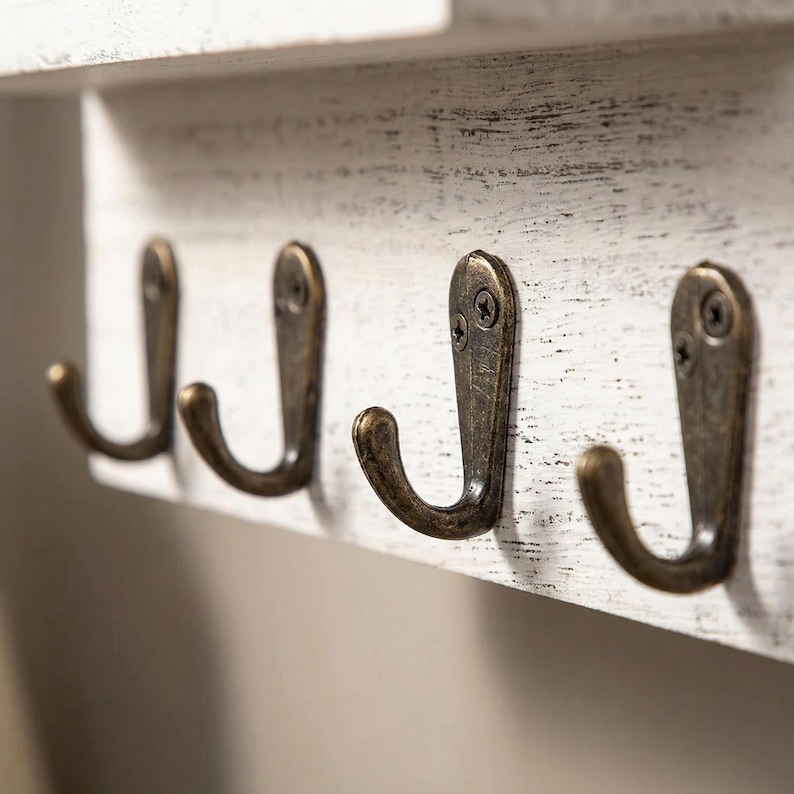 May include: A distressed white wooden wall-mounted shelf with four antique bronze metal hooks. The hooks are curved and attached with screws. The shelf has a rustic, farmhouse style.