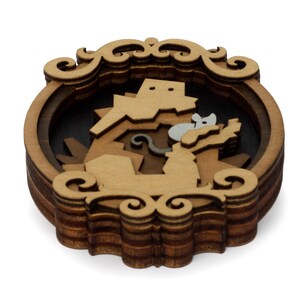 May include: A wooden layered ornament with a detailed design of a mouse and a cat. The ornament is brown and has a decorative frame.