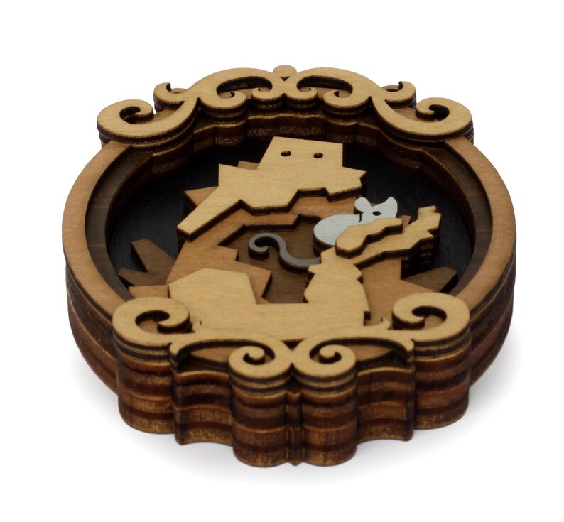 May include: A wooden layered ornament with a detailed design of a mouse and a cat. The ornament is brown and has a decorative frame.