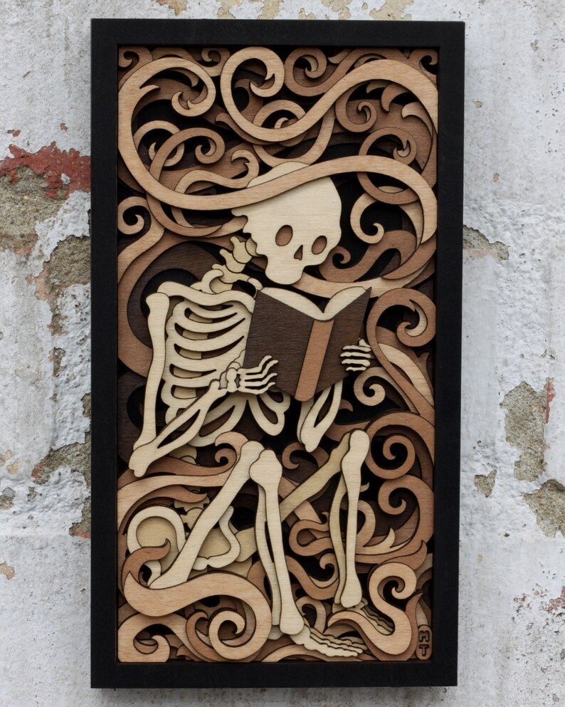 May include: A wooden wall art piece featuring a skeleton sitting and reading a book. The skeleton is surrounded by intricate, carved swirls and patterns in shades of brown.