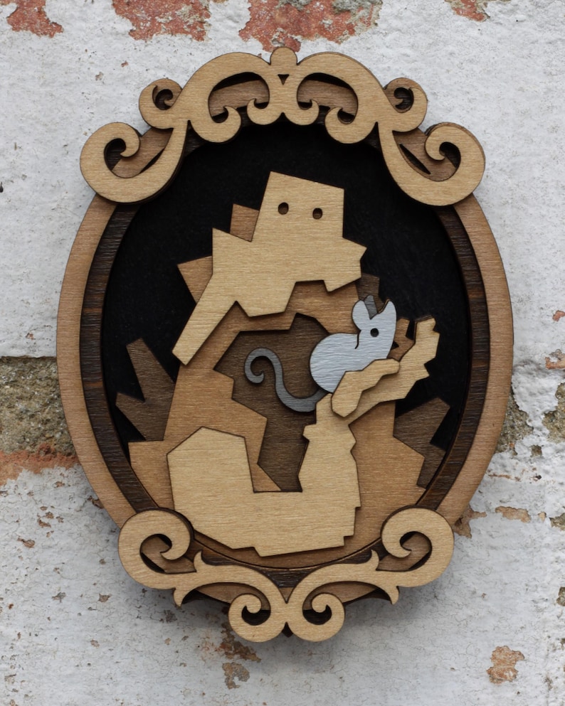 May include: A wooden wall hanging with a decorative frame. The frame is oval shaped and has a brown wood finish. The center of the frame features a cutout design of a brown and gray mouse climbing a brown structure.