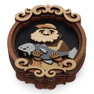 Puede incluir: Pieza de arte de madera en capas que representa a un hombre barbudo sosteniendo un pez. La obra de arte presenta una paleta de colores marr&oacute;n oscuro, marr&oacute;n claro y gris. El hombre lleva un sombrero y un delantal. La pieza est&aacute; enmarcada con volutas decorativas.