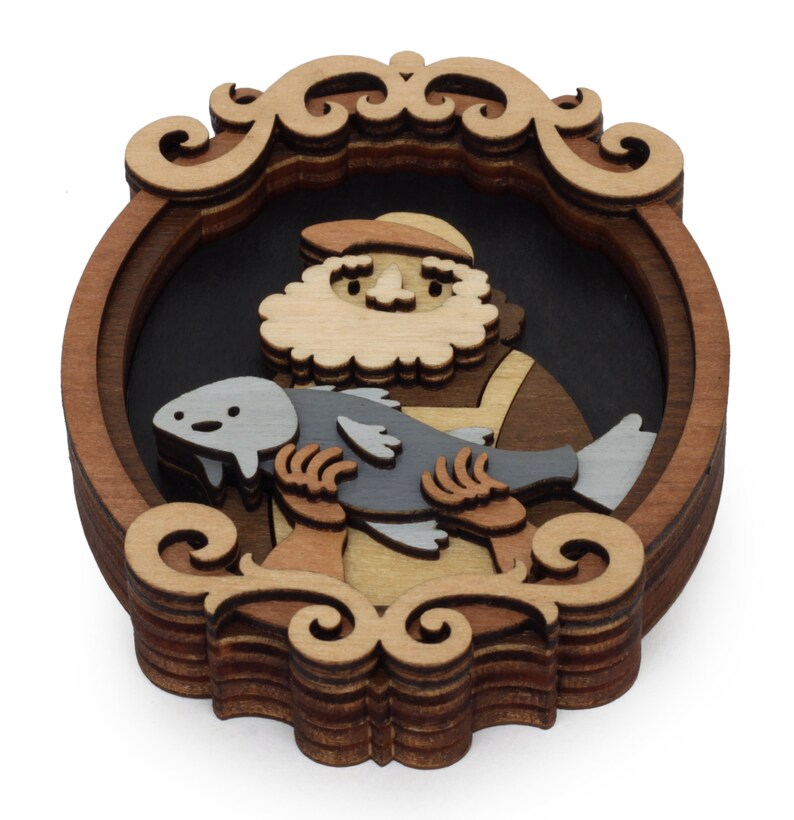 Puede incluir: Pieza de arte de madera en capas que representa a un hombre barbudo sosteniendo un pez. La obra de arte presenta una paleta de colores marr&oacute;n oscuro, marr&oacute;n claro y gris. El hombre lleva un sombrero y un delantal. La pieza est&aacute; enmarcada con volutas decorativas.