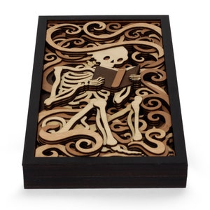 May include: A wooden wall art piece featuring a skeleton reading a book. The skeleton is surrounded by intricate swirls and patterns, creating a whimsical and spooky design.