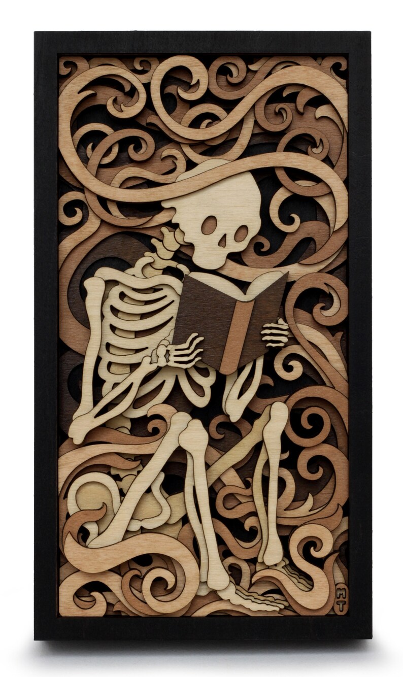 May include: A wooden wall art piece featuring a skeleton sitting and reading a book. The skeleton is surrounded by intricate, layered wood carvings of swirling patterns. The piece is framed in black wood.
