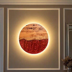 Könnte beinhalten: Ein rundes Wandkunstwerk mit einem Holzaufsatz und einem roten Harzboden. Das Stück wird von einem warmen, leuchtenden Licht an den Rändern beleuchtet. Das Holz hat ein natürliches Maserungsmuster und das Harz hat ein strukturiertes Aussehen.