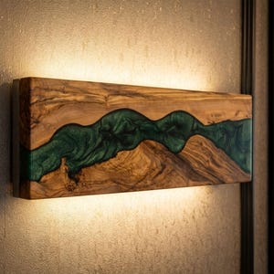 Op de afbeelding: Een rechthoekig houten wandkunstwerk met een rivierachtig ontwerp. Het kunstwerk heeft een donkergroene, vloeiende epoxyhars in een natuurlijke houten lijst. Het stuk wordt van onderaf verlicht, waardoor een warme gloed ontstaat.