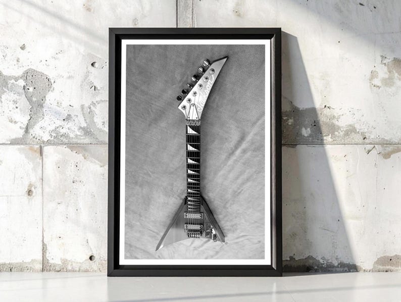 Może przedstawiać: Czarno-biała oprawiona grafika przedstawiająca gitarę elektryczną. Gitara ma korpus w kształcie litery V i gł&oacute;wkę z kołkami do strojenia. Widoczna jest podstrunnica i struny. Grafika jest na tle teksturowanego szarego tła.
