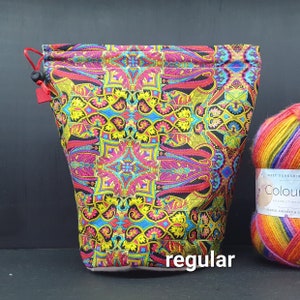 May include: A colorful yarn project bag with a drawstring closure. The bag features a vibrant paisley pattern in shades of pink, yellow, blue, and black. The word "regular" is printed on the bag. A ball of colorful yarn sits next to the bag.
