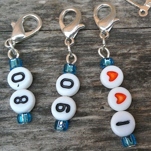 May include: Three silver keychains with blue and white beads. The beads have the numbers 0, 8, and 0 on one keychain, the numbers 0, 8, and 0 on another keychain, and a heart, a heart, and a line on the third keychain.