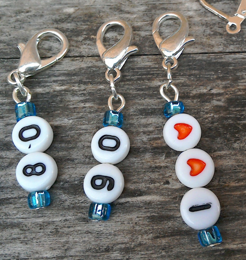 May include: Three silver keychains with blue and white beads. The beads have the numbers 0, 8, and 0 on one keychain, the numbers 0, 8, and 0 on another keychain, and a heart, a heart, and a line on the third keychain.