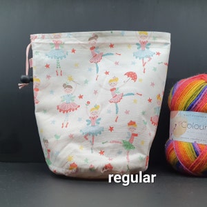 May include: A white drawstring bag with a fairy and star pattern. The bag is labeled "regular". A ball of rainbow yarn is next to the bag.