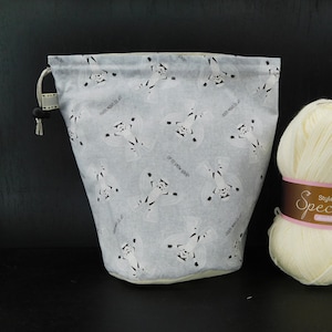 May include: A white drawstring bag with a grey and black pattern of stylized animals. The bag is filled with a ball of white yarn. The yarn label reads "Style Spectacle Hand-Dyed"
