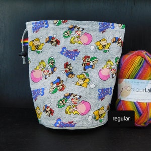 Könnte beinhalten: Eine graue Kordeltasche mit einem Super Mario 3 Muster. Die Tasche ist mit buntem Garn gefüllt.