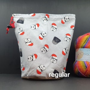 May include: A grey drawstring bag with a white background and a repeating pattern of Star Wars characters wearing Santa hats. The bag is labelled "regular".