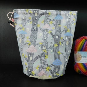 May include: A light purple drawstring bag with a whimsical design of trees, houses, and mushrooms. The bag is made of fabric and has a white drawstring.