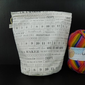 Puede incluir: Una bolsa de tela blanca con texto negro que dice "Soy un creador" e incluye una regla con pulgadas marcadas. La bolsa está llena de hilo de colores.