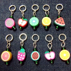 May include: Twelve colourful fruit-shaped stitch markers with silver rings and green beads. The markers include a watermelon, kiwi, orange, apple, strawberry, and a grapefruit.