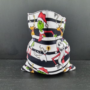 May include: A black and white striped fabric neck gaiter with a Christmas theme. The fabric features images of the Grinch, Jack Skellington, and Zero from the Nightmare Before Christmas.