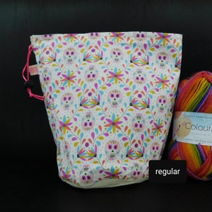 May include: A white drawstring bag with a colorful skull and flower pattern. The bag is filled with rainbow yarn. The yarn label reads "West Yorkshire Colour".