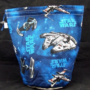 May include: A blue drawstring bag with a Star Wars theme. The bag features a repeating pattern of X-wings, TIE fighters, and the Millennium Falcon against a dark blue background with white stars. The text "STAR WARS" appears multiple times on the bag.