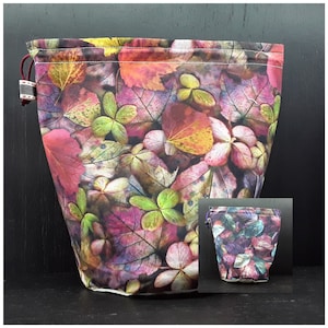 May include: A drawstring bag with a colourful leaf print. The bag is made of fabric and has a drawstring closure. The leaves are in shades of pink, purple, green, and yellow.