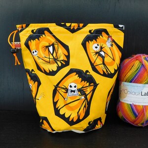 Op de afbeelding: Gele trekkoordtas met een zwart-witte print van Jack Skellington uit The Nightmare Before Christmas. De tas ligt naast een bol regenboogkleurig garen.