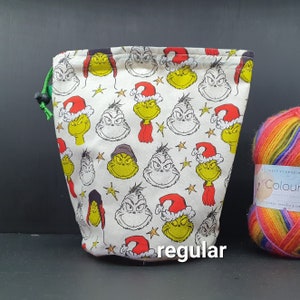Könnte beinhalten: Eine weiße Kordeltasche mit einer grünen Kordel und einem sich wiederholenden Muster des Grinch, der einen Weihnachtsmann-Hut trägt. Die Tasche ist mit "regular" beschriftet.