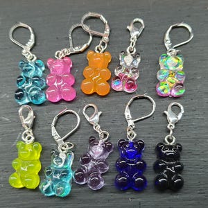 Könnte beinhalten: Ein Set mit zehn bunten Gummibärchen-Maschenmarkierern. Jeder Marker hat einen Gummibärchen-Anhänger in einer anderen Farbe, der an einem silbernen Schlüsselring befestigt ist.