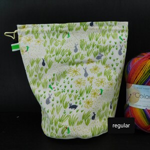 May include: White drawstring bag with a green and gray bunny rabbit pattern. The bag is made of fabric and has a drawstring closure. The bag is sitting on a black surface. The text "regular" is visible in the lower right corner of the image.