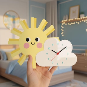 May include: A whimsical wall clock shaped like a smiling sun and a cloud. The sun is yellow with pink cheeks and a black smiling face. The cloud is white with black clock hands and blue numbers. The clock is held in a hand.