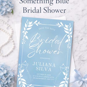Puede incluir: Una invitación a una despedida de soltera azul claro con detalles florales blancos y texto. La invitación incluye el texto "Something Blue Bridal Shower" y los detalles de la despedida de Juliana Silva el 30 de octubre de 2030.