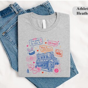 May include: An athletic heather grey t-shirt featuring a blue and pink graphic illustration of a building surrounded by speech bubbles with text including I'm going to kiss u, with tongue?, KILL U: I MEAN KILL U DANN AUTOCORRECT, and The Deal.