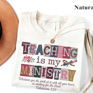May include: Cream-colored t-shirt with the words "TEACHING is my MINISTRY" in colorful, patchwork-style letters. The shirt also features the text "Whatever you do, work at it with all your heart, as working for the Lord Colossians 3:23."