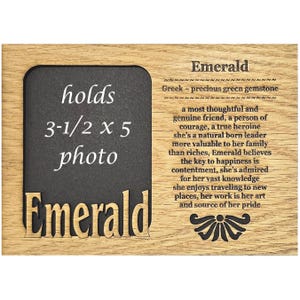 May include: A wooden plaque with a black frame that holds a 3 1/2 by 5 inch photo. The plaque is engraved with the word "Emerald" and a description of the gemstone's meaning.