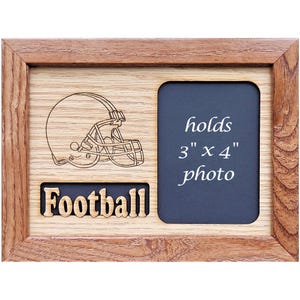 Puede incluir: Un marco de fotos de madera con un diseño de casco de fútbol y la palabra "Football" grabada en la parte inferior. El marco admite una foto de 7,6 x 10,2 cm.