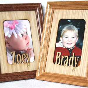 May include: Two wooden picture frames with a light brown wood finish. The frames have a cutout for a photo and a name. The left frame has a photo of a baby girl with a pink flower headband and the name "Zoey" cut out below the photo. The right frame has a photo of a young boy with blonde hair and the name "Brady" cut out below the photo.