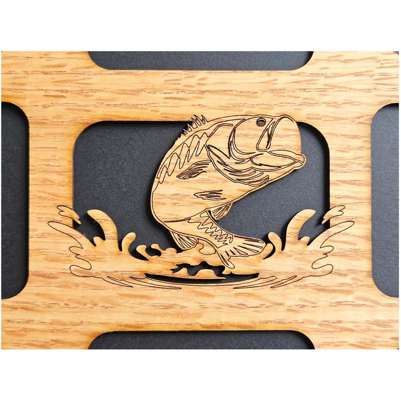 May include: A light brown wooden cutout featuring a laser-engraved largemouth bass jumping out of water. The fish is depicted in a dynamic pose with detailed scales and fins, set against a dark background within a rectangular wooden frame.
