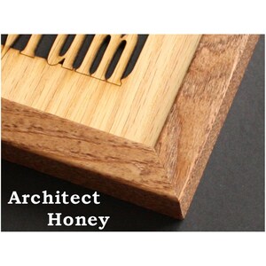 May include: A wooden frame with a mitered corner joint featuring a light-colored wood insert with laser-cut lettering. The frame has a visible natural wood grain pattern in a medium brown tone, contrasting with the lighter, smooth wood panel.