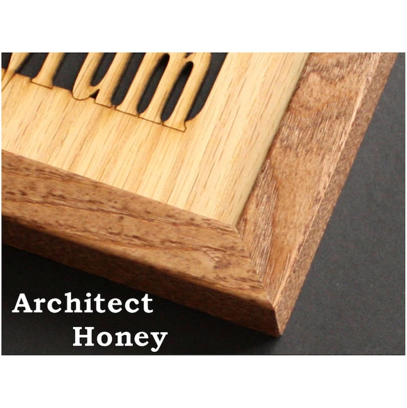 May include: A wooden frame with a mitered corner joint featuring a light-colored wood insert with laser-cut lettering. The frame has a visible natural wood grain pattern in a medium brown tone, contrasting with the lighter, smooth wood panel.